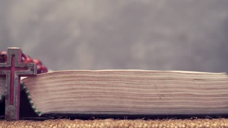 Open-Bible-and-the-crucifix-beads-on-a-golden-table,-close-up.-Beautiful-dark-background.-Religion-concept