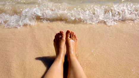 La-onda-costera-de-la-mar-en-calma-tibia-lava-dos-pies-de-una-mujer-descansando-en-la-playa.