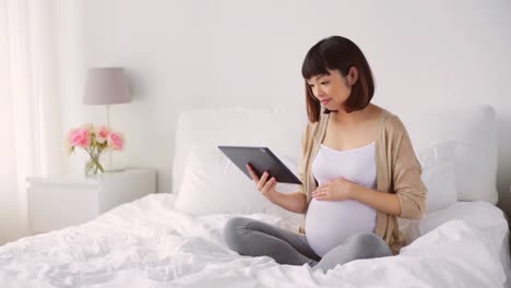happy-pregnant-asian-woman-with-tablet-pc-at-home