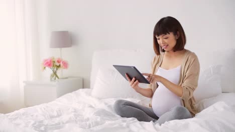 happy-pregnant-asian-woman-with-tablet-pc-at-home