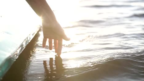 At-sunset,-close-up-the-hand-of-a-girl-moving-through-the-water