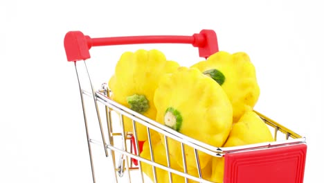 Closeup-of-supermarket-trolley-with-yellow-pattypan-squashes.-Shopping-cart-is-moving-in-the-frame.-Isolated-on-the-white-background.