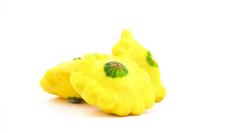 Zwei-ganze-gelbe-Patisson-Kürbisse-und-eine-halbe-Pattypan-Squash.-Auf-dem-Plattenteller-drehen.-Auf-dem-weißen-Hintergrund-isoliert.-Close-up.-Makro.