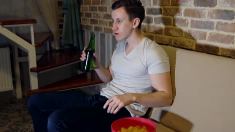 Man-drinks-beer-and-chips-in-front-of-TV-watching-football