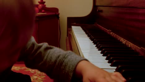 Caucasian-Toddler-Boy,-Sitting-at-a-Piano-with-Him-Mom,-Plays-on-the-Piano-with-a-decorated-Christmas-Tree-Behind-Them