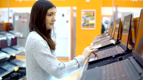 Young-brunette-woman-chooses-a-laptop-in-a-hardware-store