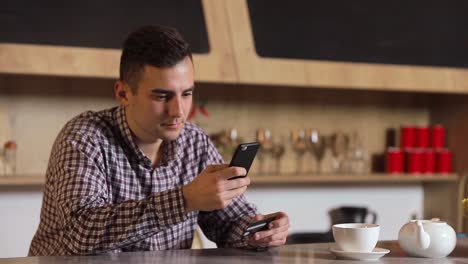 Handsome-man-making-purchase-online,-typing-credit-card-details-on-black-smartphone-in-the-modern-kitchen