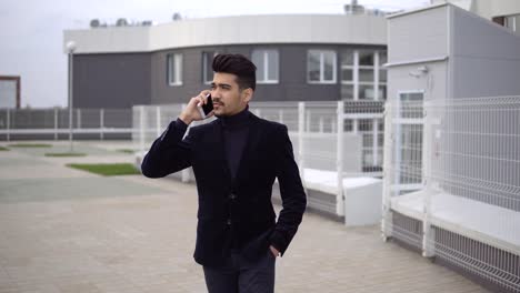 Hombre-de-negocios-joven-guapo-hablando-en-teléfono-inteligente-sonriendo-feliz-vistiendo-traje-chaqueta-al-aire-libre.