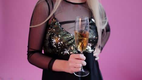 Hübsches-Mädchen-tragen-rote-Hörner,-halten-Sie-ein-Glas-Champagner-und-für-Kamera-im-Studio-rosa-Hintergrund-darstellen