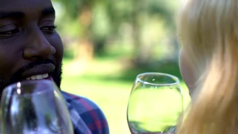 Happy-mixed-race-couple-kissing-and-clinking-glasses-with-red-wine,-close-up