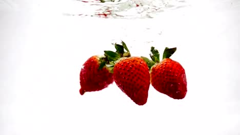 The-red-strawberry-falls-beautifully-into-the-water-with-bubbles.-Video-beryy-on-isolated-background-in-slow-motion-.