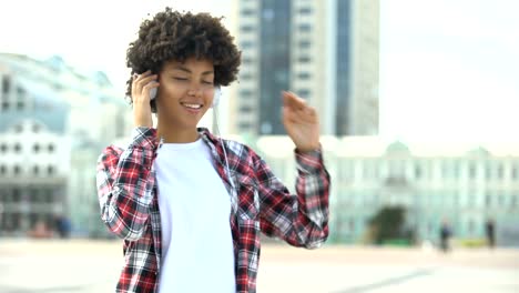 Young-curly-haired-woman-listening-to-music-in-headphones-and-singing-song