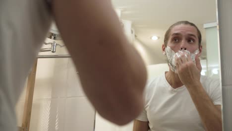 Man-Applying-Shaving-Foam-On-Face-Skin-And-Looking-In-Mirror