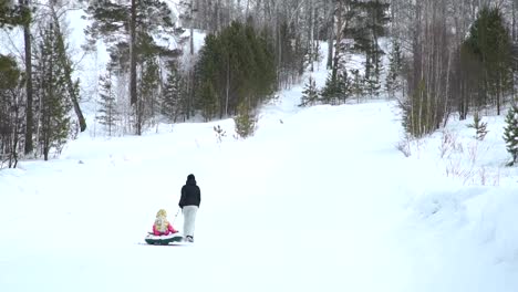 Mutter-und-Tochter-ziehen-eine-Snow-Tube-zu-einem-Hügel