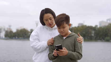 Asiática-madre-e-hijo-usando-la-aplicación-de-entrenamiento-en-Smartphone-al-aire-libre