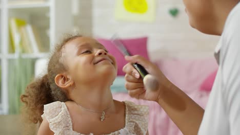 Mutter,-die-Make-up-auf-das-Gesicht-der-Tochter-aufwendet