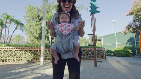 POV-coming-down-on-slide-at-park-to-meet-mother-with-baby-on-carrier