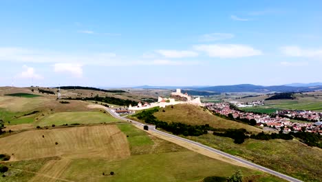 Aero.-vista-panorámica-del-antiguo-castillo,-fortaleza-de-defensa-Rupea-colocado-en-la-cima-de-una-colina.-a-los-pies-del-castillo-hay-una-pequeña-ciudad.-Transilvania,-Rumania.-día-soleado-de-verano-caliente