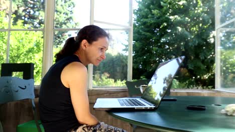 Casual-candid-shot-of-woman-yawning-in-front-her-computer-screen.-Mother-in-her-30s-working-from-her-balcony-home.