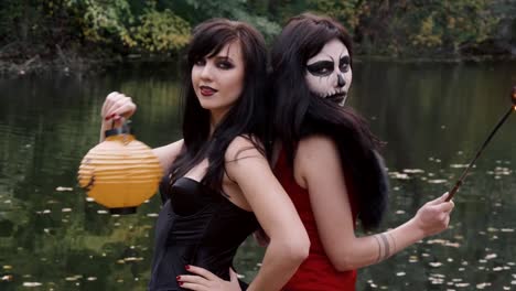 Young-halloween-girl-friends-in-black-and-red-witch-dress-having-fun-in-the-forest-park-with-traditional-autumn-holiday-symbol-of-orange-spooky-pumpkin-outdoor