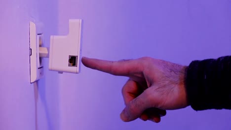 Menschen-drücken-mit-dem-Finger-auf-die-WPS-Taste-am-WLAN-Repeater-in-die-Steckdose-an-der-Wand