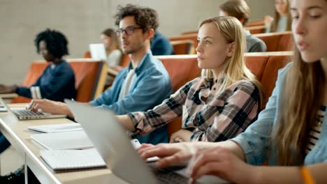 In-die-Klassenzimmer-Multi-ethnischen-Studenten,-Verwendung-Laptops-während-der-Wiedergabe-als-Dozent.-Einige-schreiben-in-Notebooks.-Helle-Jugendliche-Studium-an-der-Universität.