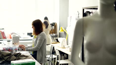 Vista-lateral-del-joven-sastre-mujer-trabajando-con-la-máquina-de-coser-en-luz-sastrería.-Mujer-es-ajuste-de-equipo-y-costura-textil-cuidadosamente.