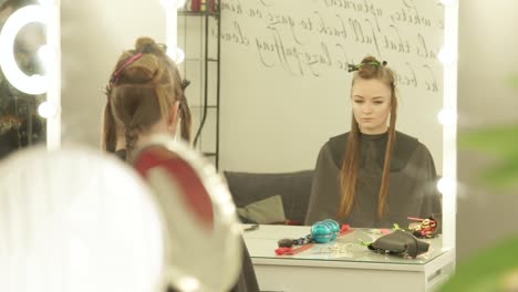 Young-woman-with-clip-for-fixing-long-hair-during-hairdressing-sitting-in-chair-front-mirror-in-beauty-studio.-Woman-hair-model-in-hairdessing-salon