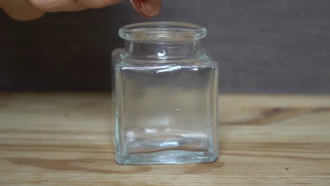 Business-concept---man-hand-throw-euro-coins-into-little-transparent-jar.