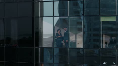 Aerial-Footage-From-Outside-of-the-Skyscraper:-Businessman-and-Businesswoman-Talking-Business-while-Standing-in-the-Office-Window.-Flying-Shot-of-the-Financial-Business-District-and-Businesspeople-Working-in-the-Big-City.