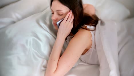 Young-brunette-woman-wakes-up-from-ring-of-a-mobile-phone,-and-speaks-phone.