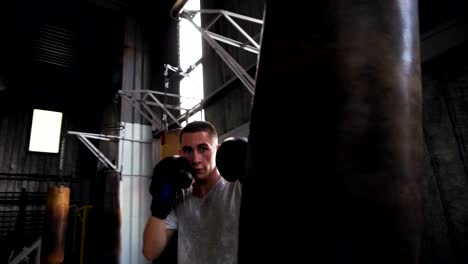 Close-up-footage-of-a-male-boxer-working-out-in-gym,-training-process-with-punching-bag.-Boxer-in-black-boxing-gloves,-white-T-shirt