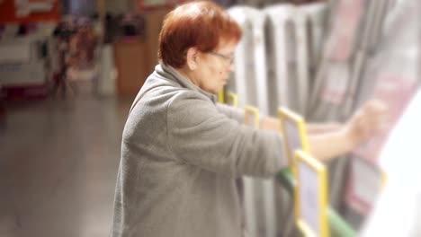 An-elderly-woman-chooses-a-ladder-to-the-house-construction-hypermarket