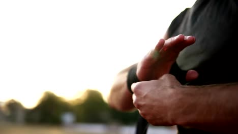 Hands-of-young-wrapping-hands-with-bandages-for-workout-in-summer-day-outdoors.-Muscular-young-boxer-in-black-T-shirt.-lurred-background