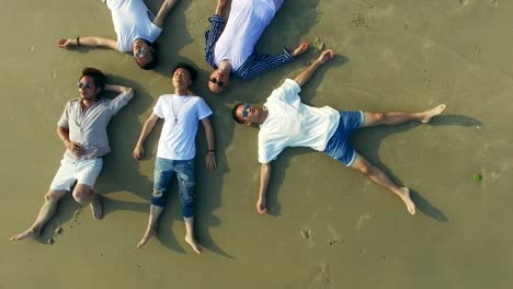 young-asian-adults-lying-on-back-on-sand-beach-eyes-closed