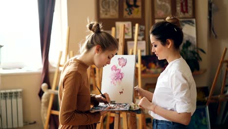 Pretty-woman-painting-teacher-is-teaching-young-girl-to-mix-paints-on-palette-creating-beautiful-color-during-art-class-in-nice-modern-studio.-People-and-education-concept.