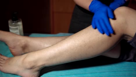 A-cosmetologist-applies-a-special-cream-on-the-female-leg-before-epilation.