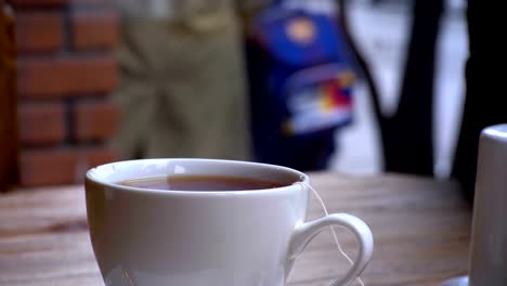 Weiße-Tasse-heißen-Tee-auf-dem-Tisch-in-einem-Cafe-auf-dem-Hintergrund-des-Fensters-Straße