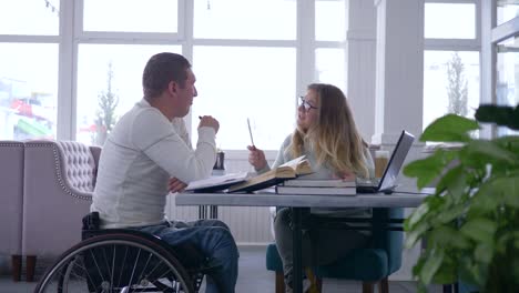 teaching-for-invalid,-happy-ill-student-male-in-wheelchair-with-educator-woman-during-home-studying-using-laptop-computer