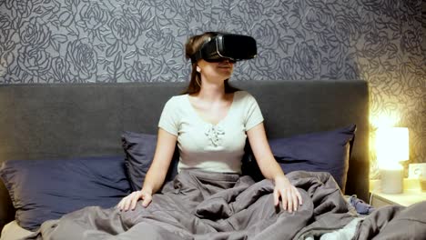 Beautiful-young-woman-wearing-VR-Headset-on-the-bed.-Looking-around,-smile-and-wave-away-with-hands.