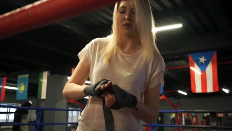 Attractive-girl-stands-in-the-ring-and-unwinds-boxing-bandages