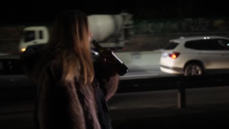 A-beautiful-drunk-woman-goes-along-the-city's-night-road-and-drinks-wine-from-the-bottle-4k-Slow-Mo