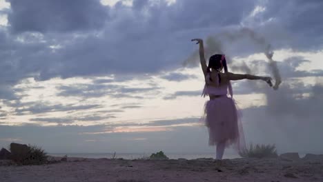 Hermosa-joven-con-maquillaje-brillante-en-un-vestido-rosado-bailando-con-bombas-de-humo-al-aire-libre.-El-baile-de-una-chica-sensual-con-un-peinado-maravilloso-con-flores.-Cámara-lenta.