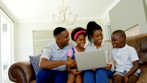 Vista-frontal-de-la-familia-joven-negro-sentado-en-el-sofá-y-usando-la-laptop-en-una-casa-confortable-4k