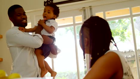 Front-view-of-young-black-father-holding-his-son-and-talking-with-mother-in-kitchen-at-home-4k