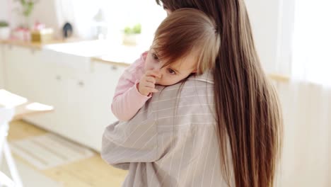 Caring-young-mom-holding-and-stroking-her-adorable-baby-daughter-lying-on-her-shoulder