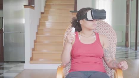 Hübsche-afroamerikanische-Frau-sitzt-auf-dem-Sessel-zu-Hause-in-der-Virtual-Reality-Headset