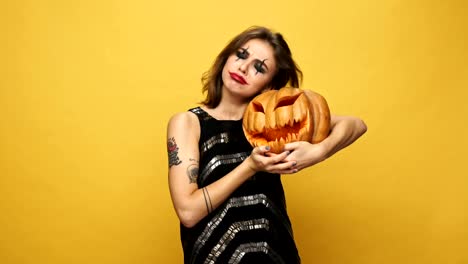 Young-pretty-funny-lady-with-scary-make-up-hugging-with-pumpkin-isolated-over-yellow