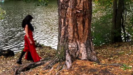 Woman-with-scary-halloween-make-up-in-red-dress-walking-in-the-forest-park-beetween-the-trees