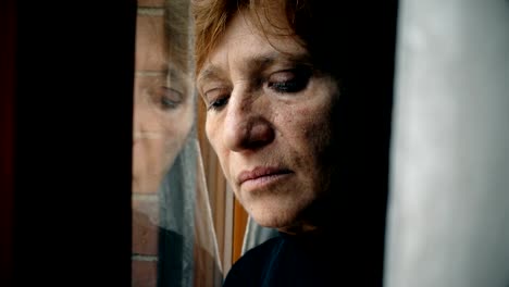 Close-up-on-sad-and-depressed-mature-woman-leaning-against-the-window